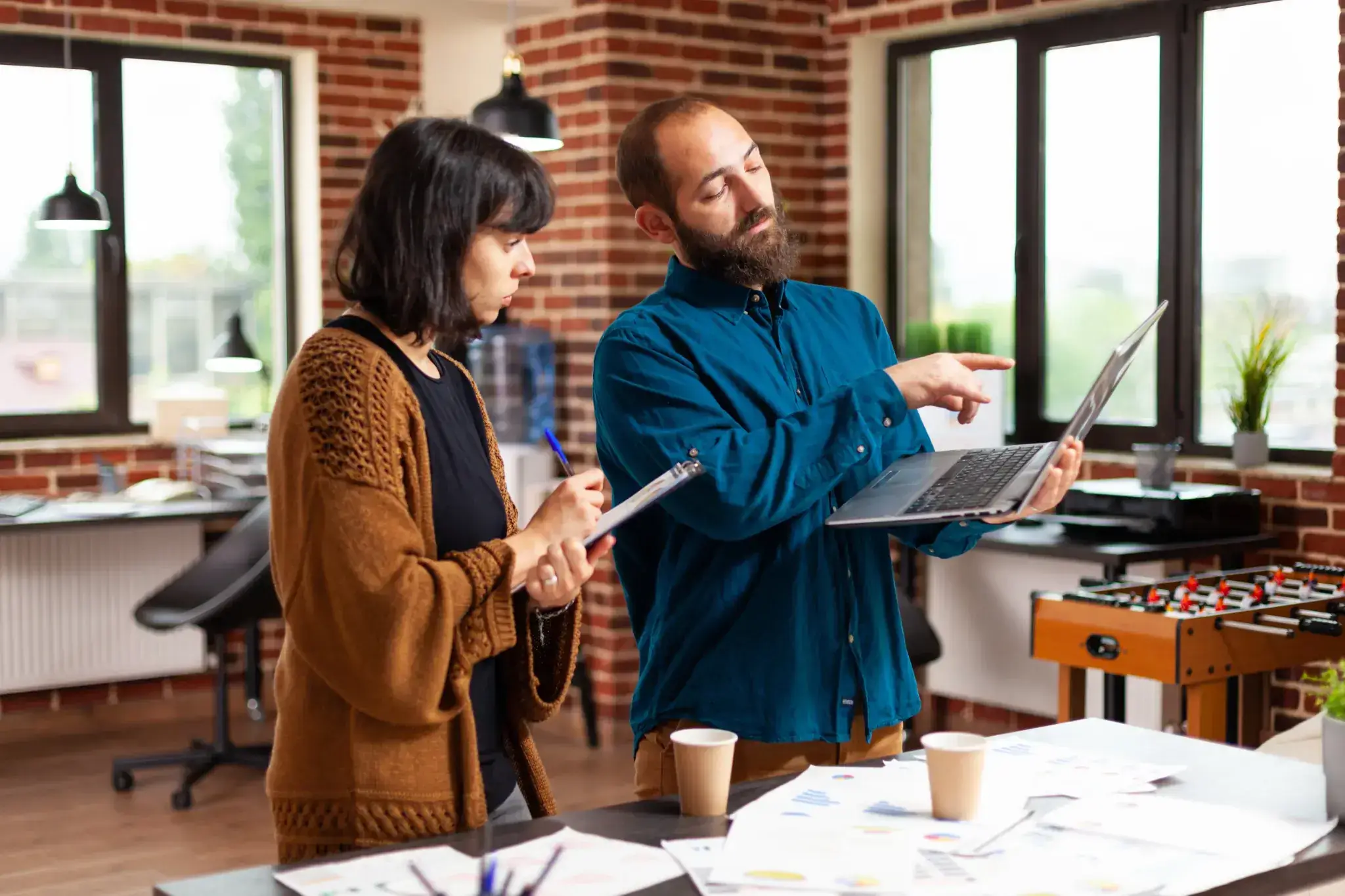 Two business professionals discussing marketing strategy in a modern office with brick walls, laptop, and documents on the table